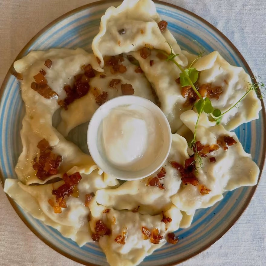 Talerz pierogów ze skwarkami i miseczką śmietany, widok z góry